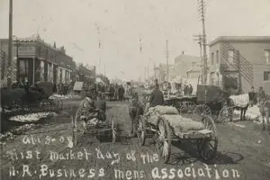 black and white photograph of horse-drawn wagons on a busy dirt road