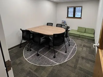 small room with table, 6 rolling chairs and small green seating area in corner