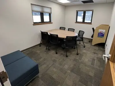small room with table, 6 rolling chairs, corner workstation, and soft seating